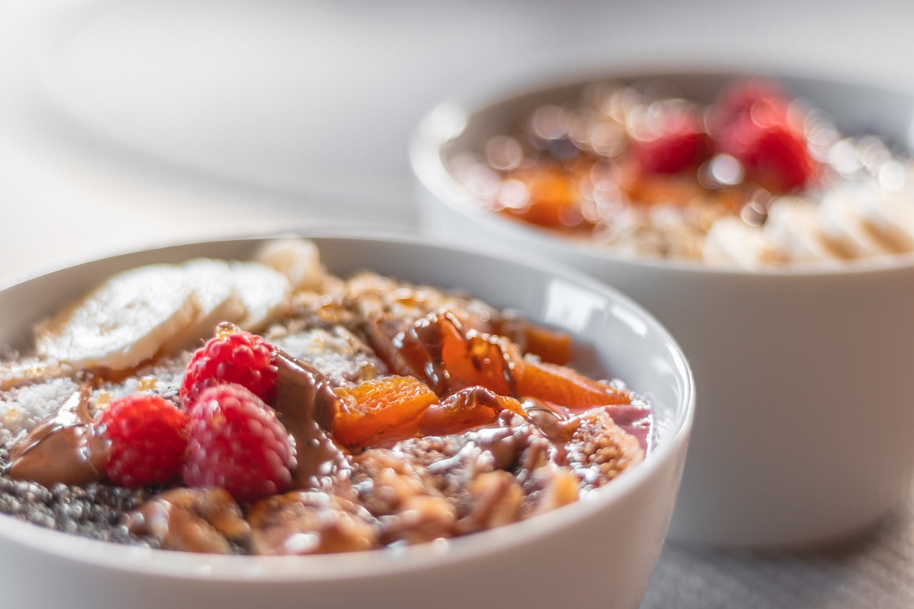 Eine gesunde Frühstücksbowl mit frischen Himbeeren, Bananenscheiben, Nüssen, Chiasamen und einer cremigen Schokoladensauce – perfekt für einen energiereichen Start in den Tag.