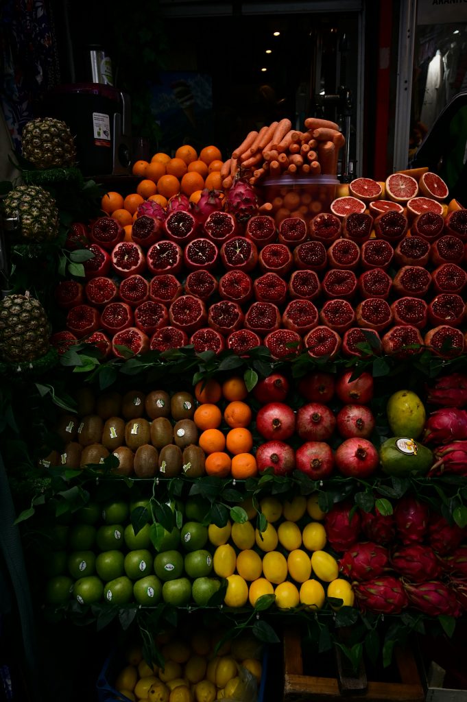 Ein lebendiger Obst- und Gemüsestand mit einer bunten Auswahl an Granatäpfeln, Orangen, Karotten, Kiwi, Ananas und weiteren frischen Früchten – perfekt für gesunde Ernährung.